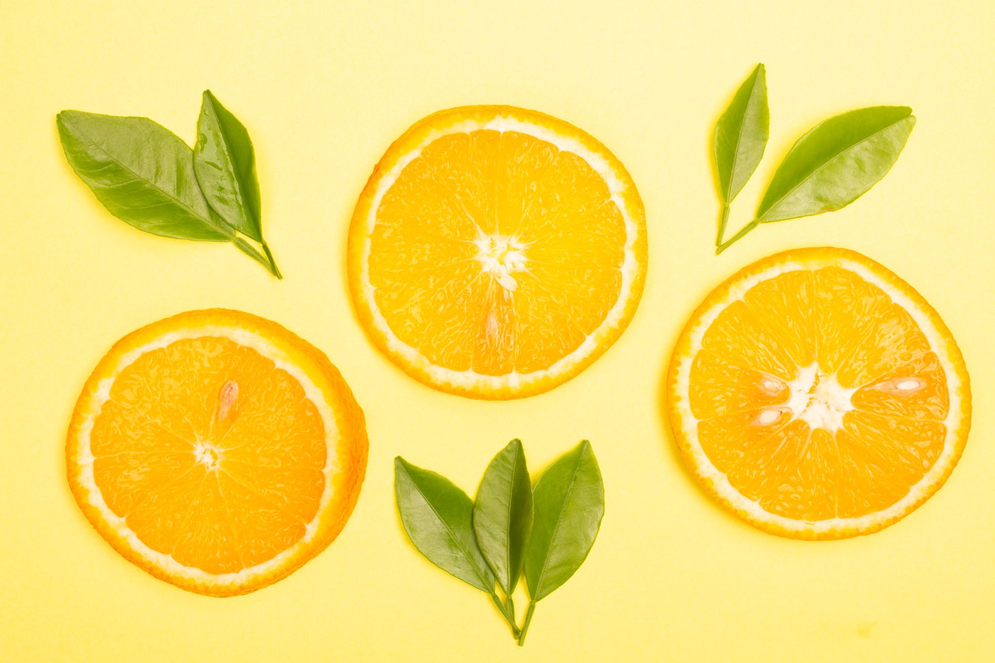 Orange slices and green leaves on a yellow background